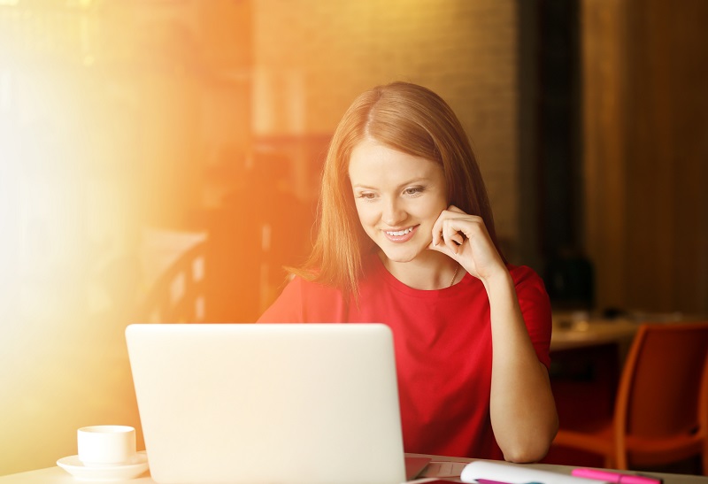 a person in a red shirt looking at a laptop.