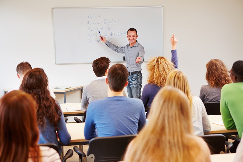 a person standing in front of a whiteboard with a group of people in the background.